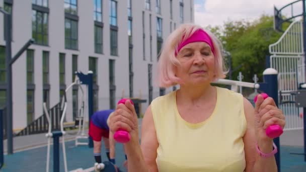Senior kvinna mormor idrottsman gör rutin tyngdlyftning hantlar övningar på lekplatsen — Stockvideo