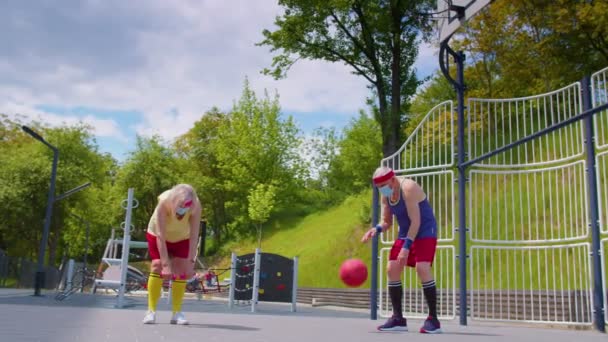 Активная пожилая женщина играет в баскетбол на открытом воздухе на спортивной площадке во время коронавируса — стоковое видео