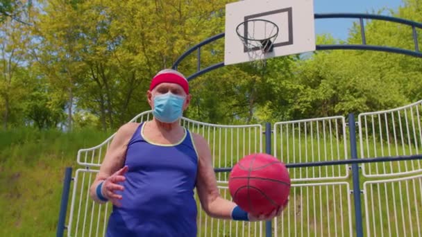 Homem bonito sênior ativo jogando basquete ao ar livre no campo de jogos esportivos durante coronavírus — Vídeo de Stock