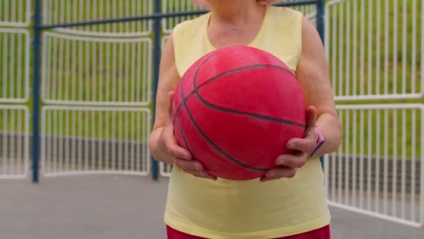 Senior γυναίκα γιαγιά αθλητής θέτει παίζει με μπάλα σε εξωτερικούς χώρους στο γήπεδο μπάσκετ παιδική χαρά — Αρχείο Βίντεο