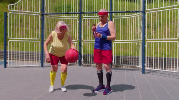 Seniorentrainer bringt Großmutter mit Basketball-Dribbelübung mit Ball auf Spielplatz bei — Stockvideo