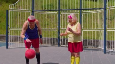 Kıdemli kadın koç büyükbabaya basketbol topuyla top sürme egzersizi öğretiyor.