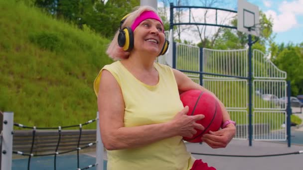Seniorbestemor etter idrettstrening med lyttemusikk på lekeplassen – stockvideo