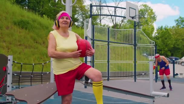 Mulher sênior avó após esporte basquete treinamento sentado ouvir música no pátio do parque infantil — Vídeo de Stock
