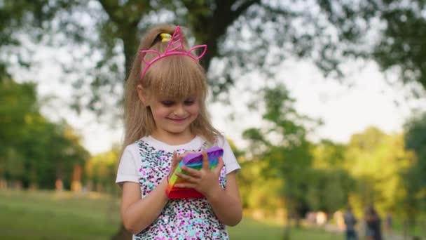 Μικρό κομψό κορίτσι παιδί παίζει πολύχρωμο squishy φυσαλίδες σιλικόνης αισθητηριακές ποπ παιχνίδι στο πάρκο — Αρχείο Βίντεο