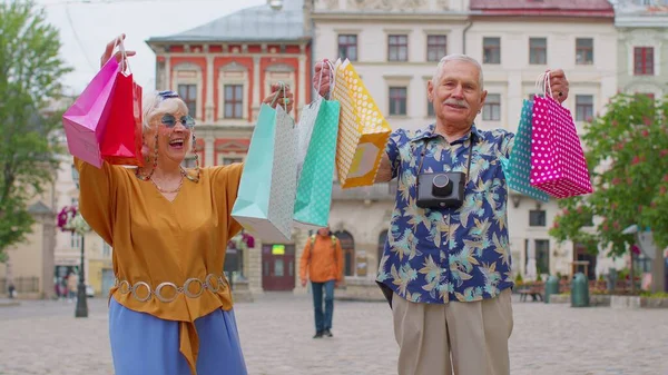 Senior oude stijlvolle toeristen man vrouw loopt met kleurrijke tassen na het winkelen in het winkelcentrum op straat — Stockfoto