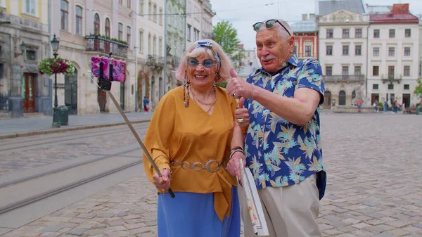 Старший старий турист чоловік з жінкою, що йде містом зі смартфоном на паличці селфі і фотографує — стокове фото