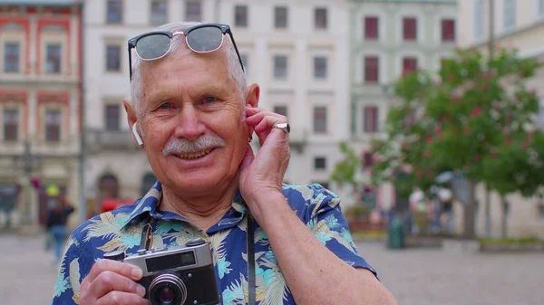 Idősebb férfi turista retro fényképezőgép, mosolygós, zenét hallgatni fülhallgató, tánc az utcán — Stock Fotó