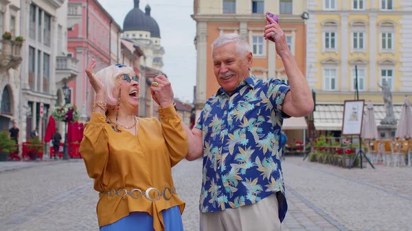 Senior oude stijlvolle toeristen op zoek smartphone oprecht blij winnen, bericht met goed nieuws — Stockfoto