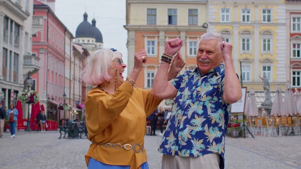 Ouderen stijlvol paar toeristen man vrouw vieren succes win schreeuw verheugt zich doen winnaar gebaar — Stockfoto