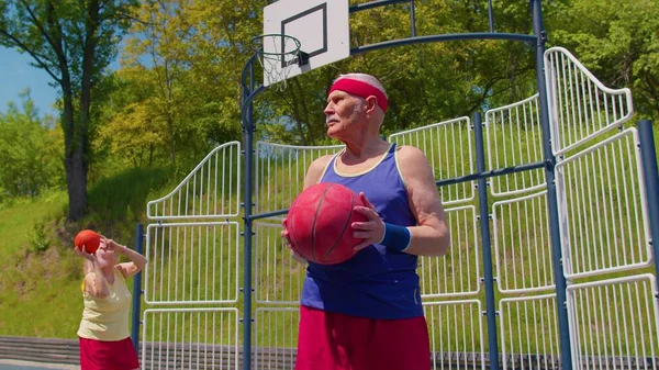 Hombre mayor abuelo posando con pelota, mirando a la cámara al aire libre en cancha de baloncesto — Foto de Stock