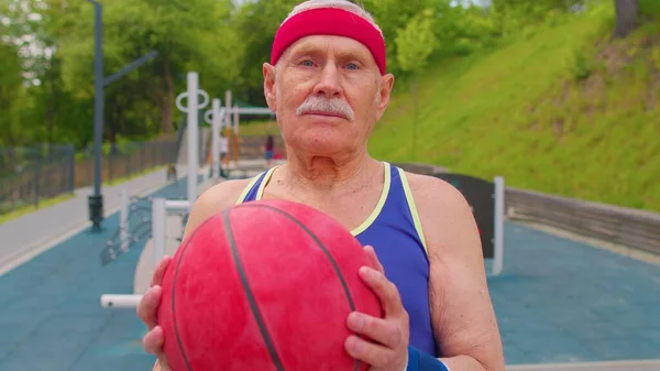 Anciano anciano abuelo atleta posando jugando con pelota al aire libre en cancha de baloncesto — Foto de Stock
