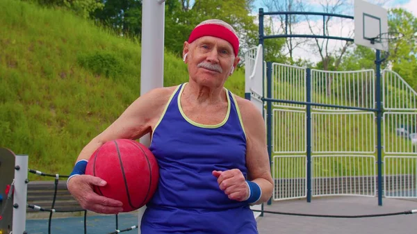 Hombre mayor abuelo después de entrenamiento de baloncesto deportivo sentado, escuchando música en la cancha de juegos —  Fotos de Stock