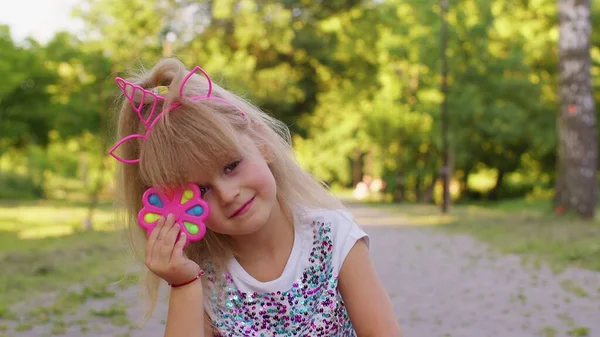 Chica feliz jugando, girando con pop it sensorial juguete anti-estrés en el parque, alivio de la ansiedad de estrés — Foto de Stock
