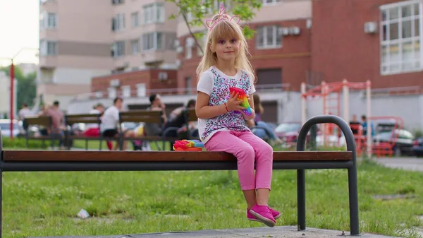 Elegante niño pequeño jugar con el pop de moda burbuja juego de juguete sensorial blando en el banco del patio — Foto de Stock