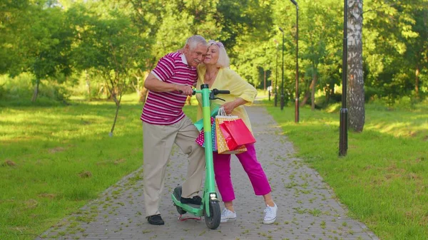 Sénior elegante casal avó, avô depois de fazer compras com sacos usando scooter para andar — Fotografia de Stock