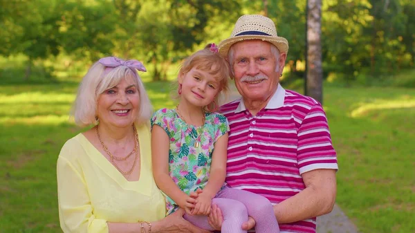 Маленькая милая внучка обнимается со своей бабушкой и дедушкой семейной парой в парке — стоковое фото