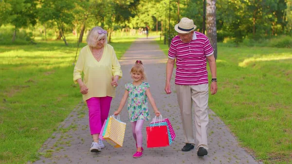 Niña niña caminando con el abuelo jubilado mayor abuela con bolsas de colores después de ir de compras — Foto de Stock