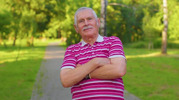 Happy lovely senior old gray-haired grandfather in casual red t-shirt on summer park background — Stockfoto