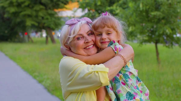 Little granddaughter child embracing kissing with her grandmother in park, happy family relationship — Stock Photo, Image