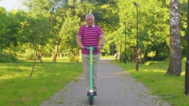 Son sınıf stil sahibi büyükbaba parkta elektrikli scooter kullanıyor, modern büyükbaba şehir aracını kullanıyor.
