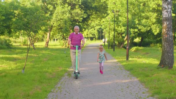 Hombre mayor moderno abuelo turista montar scooter eléctrico con nieta niña en el parque — Vídeo de stock