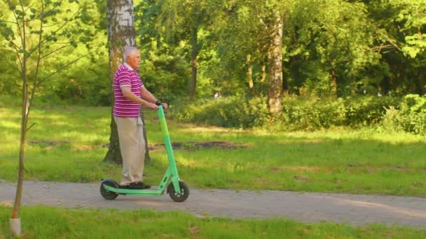 Caucasiano velho de cabelos grisalhos homem elegante avô montando scooter elétrico no parque de verão — Vídeo de Stock