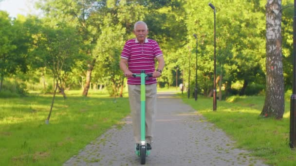 Старший стильний чоловік дідусь їде на електричному скутері в парку, сучасний дідусь за кермом міського транспорту — стокове відео