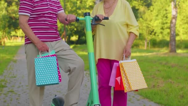 Idosos elegante casal avó, avô depois de fazer compras com sacos usando scooter para montar — Vídeo de Stock