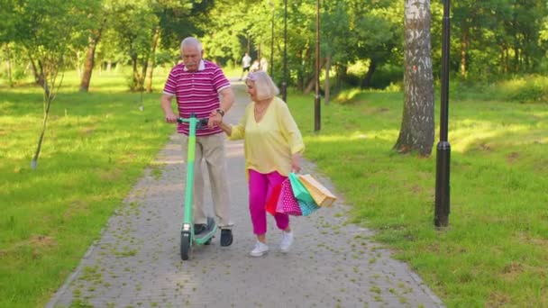 Sénior elegante casal avó, avô depois de fazer compras com sacos usando scooter para andar — Vídeo de Stock