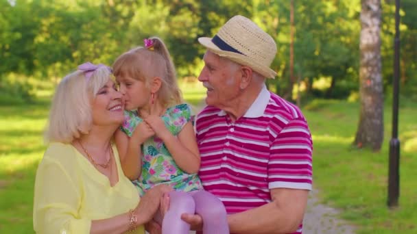 Little cute granddaughter child embracing with her grandmother and grandfather family couple in park — Stockvideo