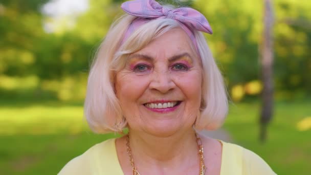 Joyeux beau senior vieille grand-mère aux cheveux gris en chemisier jaune décontracté sur fond de parc d'été — Video