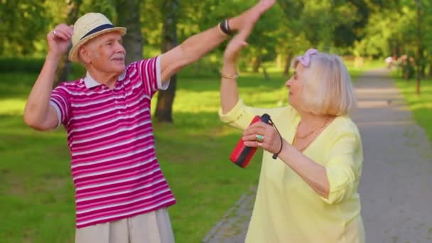 Joyful old retired family grandmother grandfather dancing listening music on musical speaker in park — Stockvideo