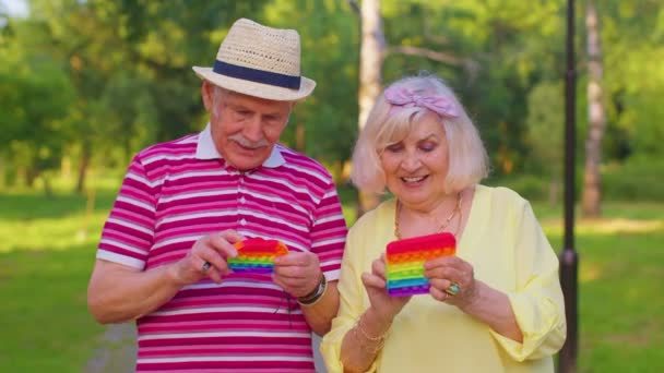 Lächelnde ältere Großmutter Großvater spielt Anti-Stress-Touchscreen-Push-Pop-es beliebtes Spielzeug — Stockvideo