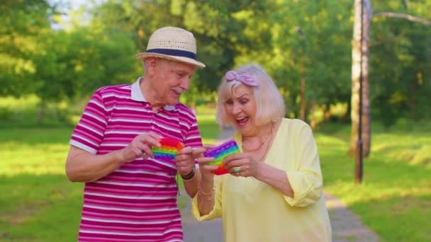 Старшая стильная пара бабушка дедушка сжимая анти-стресс толчок поп популярной игрушечной игры — стоковое видео