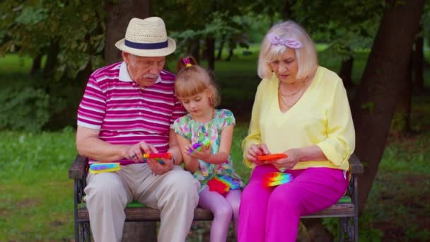 Senior stylish couple grandmother grandfather with granddaughter play anti-stress pop it toy game — Stockvideo