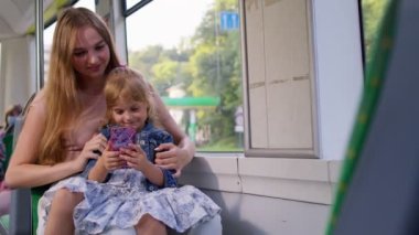 Anne ve kızı otobüsle eve gidiyor, akıllı telefonla oynuyor, sosyal medyada geziniyor.