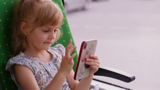 Attrayant enfant souriant fille enfant dans le train de la ville, tram ou bus en utilisant smartphone bavarder avec des amis — Video