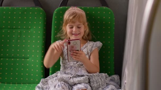 Дитяча дівчина в міському автобусі або трамвайному транспорті використовує мобільний телефон щиро радіючи перемозі, хороші новини — стокове відео