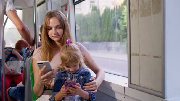 Niño niña con madre usando el teléfono móvil chatear en las redes sociales en el tranvía lleno de gente, autobús o tren — Vídeo de stock