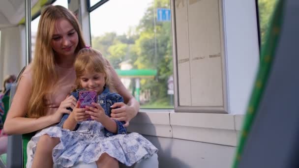 Madre con hija viajando en autobús a casa, jugando en el teléfono inteligente, navegando por las redes sociales — Vídeo de stock