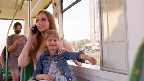 Mujer joven de la familia con niña sentada en el transporte público en autobús, madre hablando por teléfono móvil — Vídeo de stock