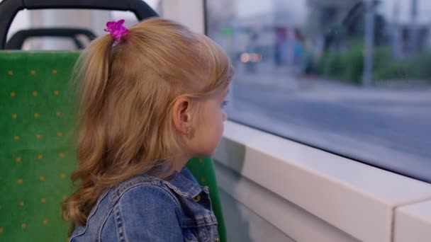 Wesoły słodkie dziecko dziewczyna pasażera jazdy w publicznym nowoczesnym autobusem lub tramwajem transportu, patrząc przez okno — Wideo stockowe