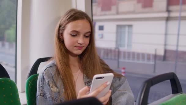 Chica joven que utiliza el teléfono móvil de Internet aplicación de red social mientras viaja en autobús en la ciudad — Vídeo de stock