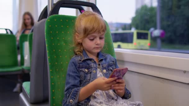 Akıllı telefondaki küçük kız, şehirde otobüsle seyahat ederken mesajlaşıyor, sosyal medyada geziniyor. — Stok video