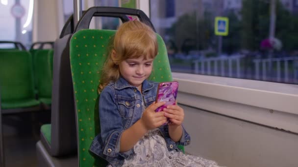 スマートフォンで遊ぶ女の子,チャット,テキストメッセージ,市内へのトラムで旅行中にソーシャルメディアを閲覧 — ストック動画