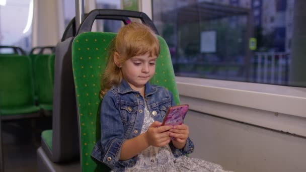 Ung lille barn pige barn i byen tog, sporvogn eller bus ved hjælp af smartphone chatter med venner – Stock-video