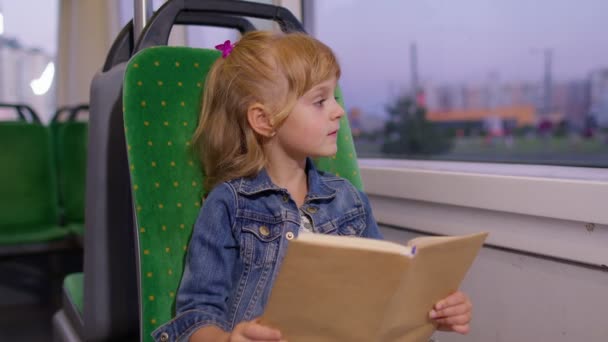 Портрет привабливої маленької дівчинки-дівчинки, яка сидить у порожньому потязі метро, читаючи цікаву книгу — стокове відео
