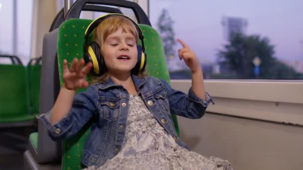 Kulaklık takan küçük kız müzik dinliyor, şehirde otobüsle seyahat ederken dans ediyor. — Stok video