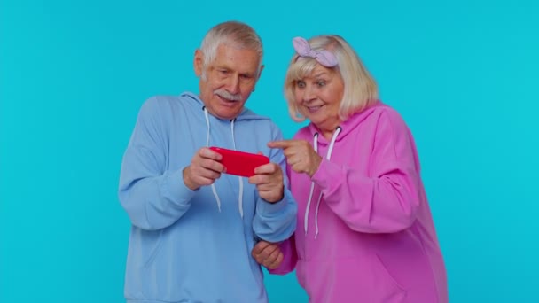 Funny senior elderly modern grandfather grandmother playing drive simulator video game on smartphone — Stock Video